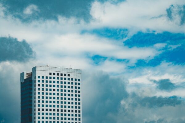 Fragment of exterior of modern skyscraper with white facade and glass windows against cloudy blue sky