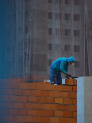 Side view of unrecognizable male in hoodie building brick wall while working on construction site in city