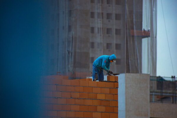 Side view of unrecognizable male in hoodie building brick wall while working on construction site in city